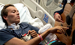 Image: Chris plucks a guitar string while recovering at UF Health Jacksonville.