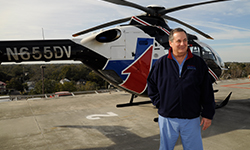 Image: David Vukich, MD, FACEP, stands next to the TraumaOne helicopter that has his initials "DV" to mark his role in its establishment.