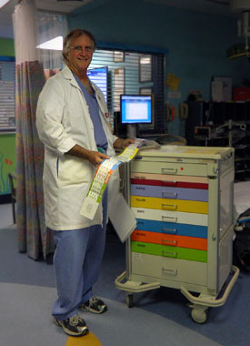 Image: Robert Luten, MD, holds the pediatric tape he co-created. Next to him is a cart with color-coded drawers that contain the appropriate equipment for the corresponding color zones on the tape.